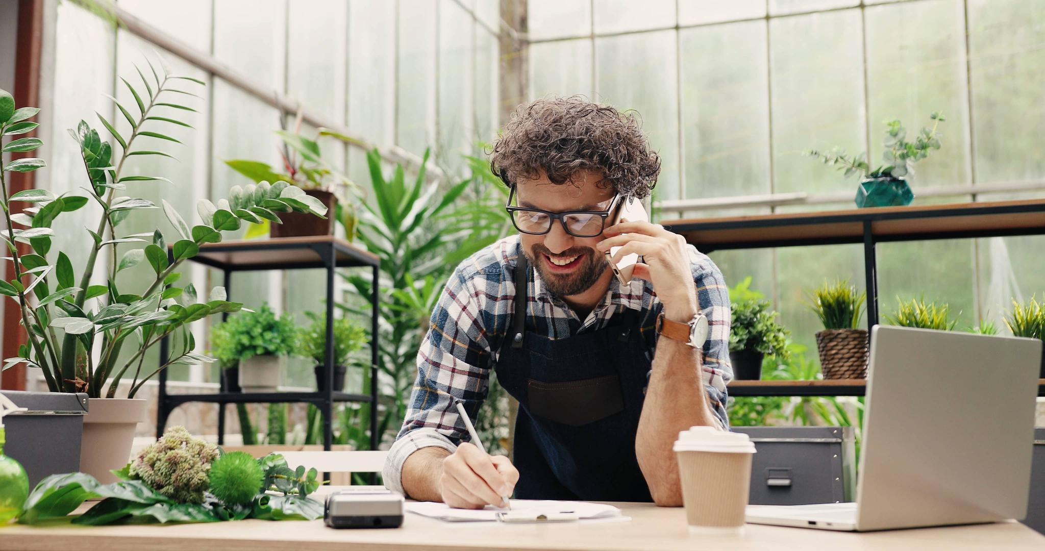 Hombre hablando por celular y escribiendo en una tienda de plantas